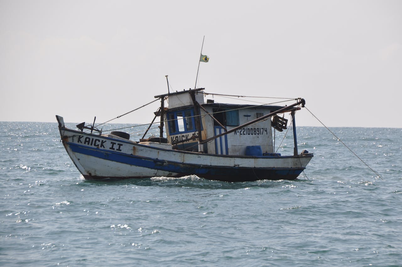 A rustic fishing boat flying the Brazilian flag is captured sailing on the open sea with a clear horizon.